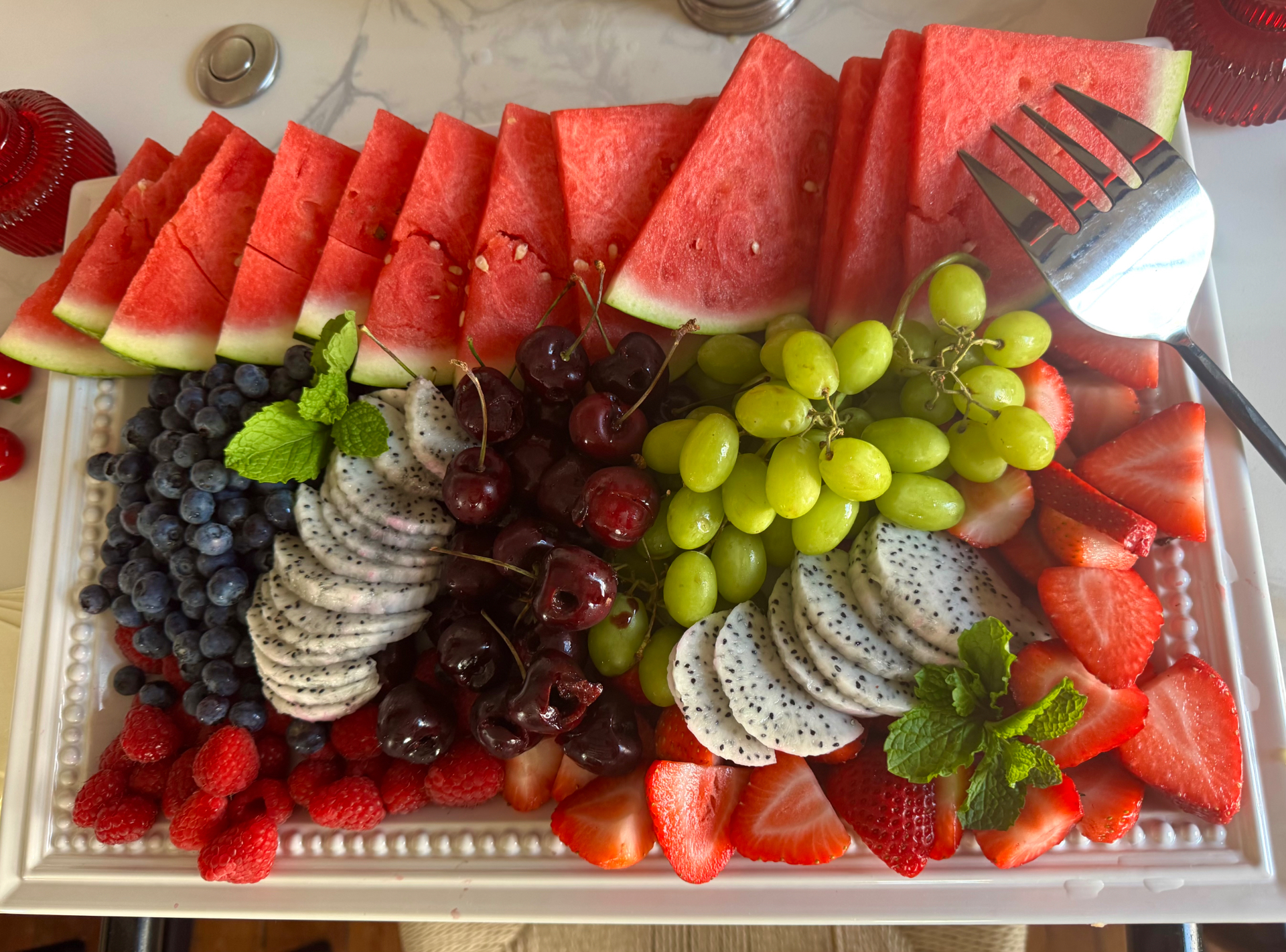 An overflowing brunch fruit platter with watermelon, berries, cherries, dragon fruit, and mint