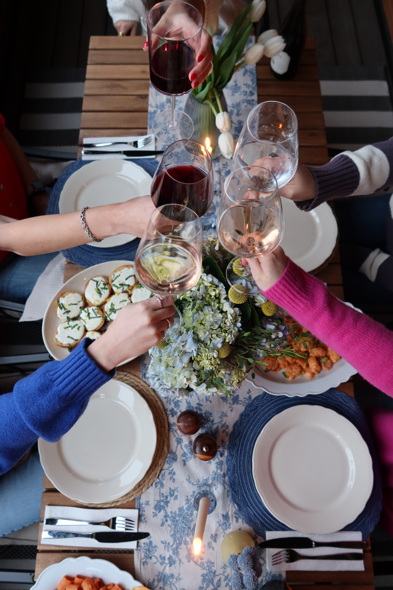 Friends toasting wine glasses above a candlelit table of shared plates