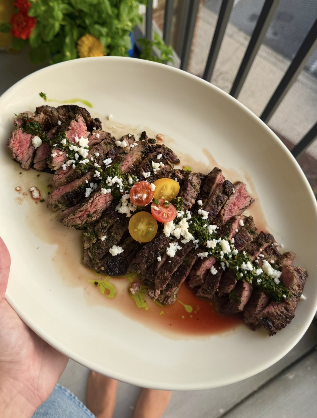 Sliced grilled steak with chimichurri, feta and heirloom tomatoes on a white platter