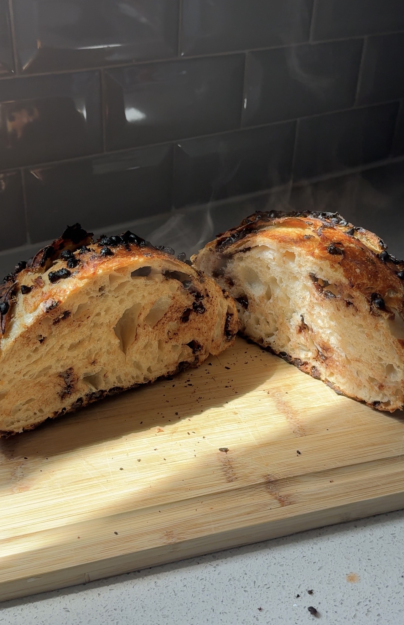 Halved loaf of chocolate studded sourdough steaming on a wooden board