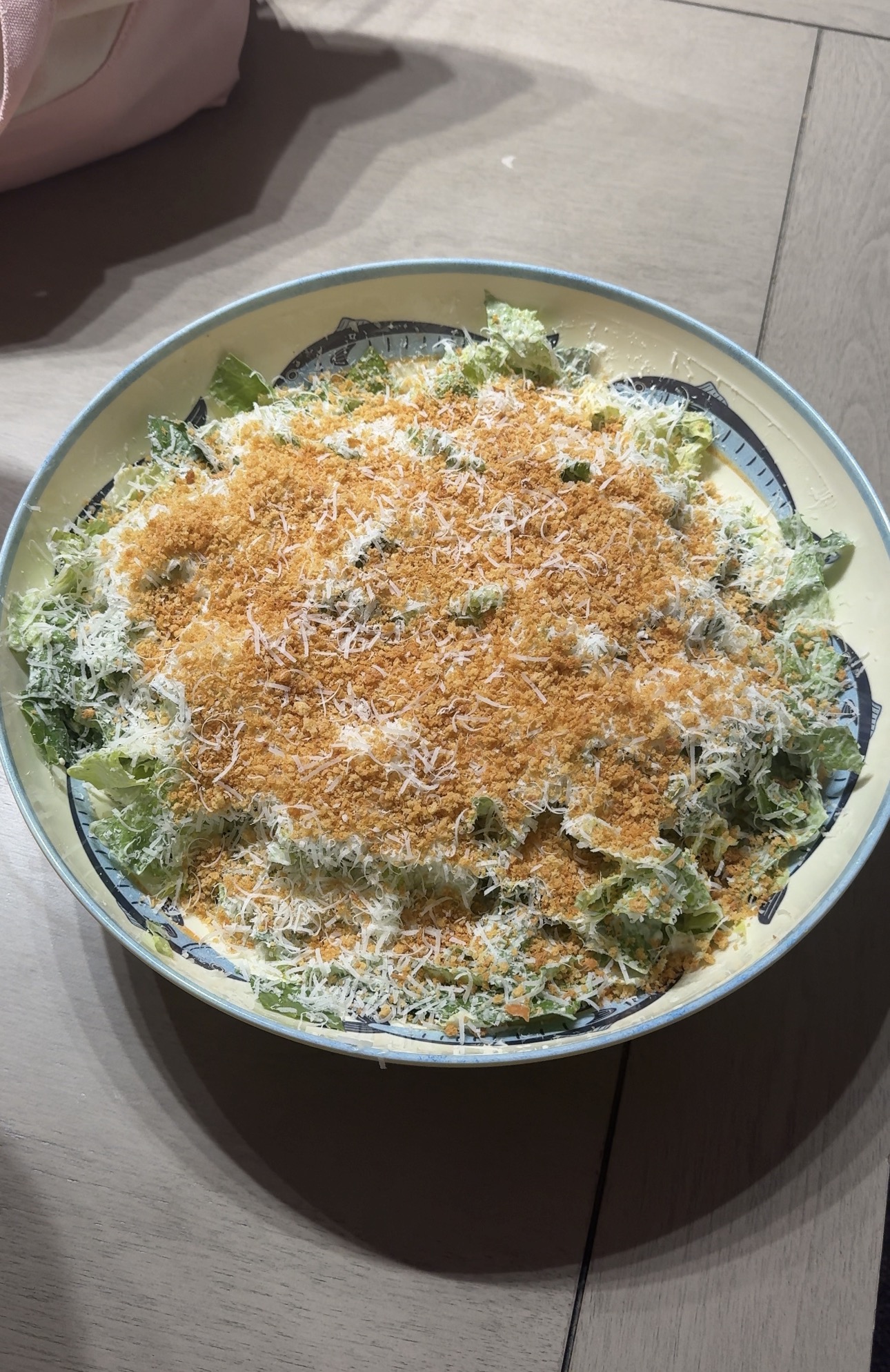 Caesar salad topped with shaved parmesan and golden breadcrumbs in a ceramic bowl